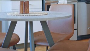 Een moderne keuken met een magnetron, oven en koffieapparaat. Er staat een eettafel met stoelen en een decoratieve vaas.