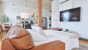 Een moderne slaapkamer met een groot bed, een leren bank, een televisie en een kitchenette op de achtergrond.