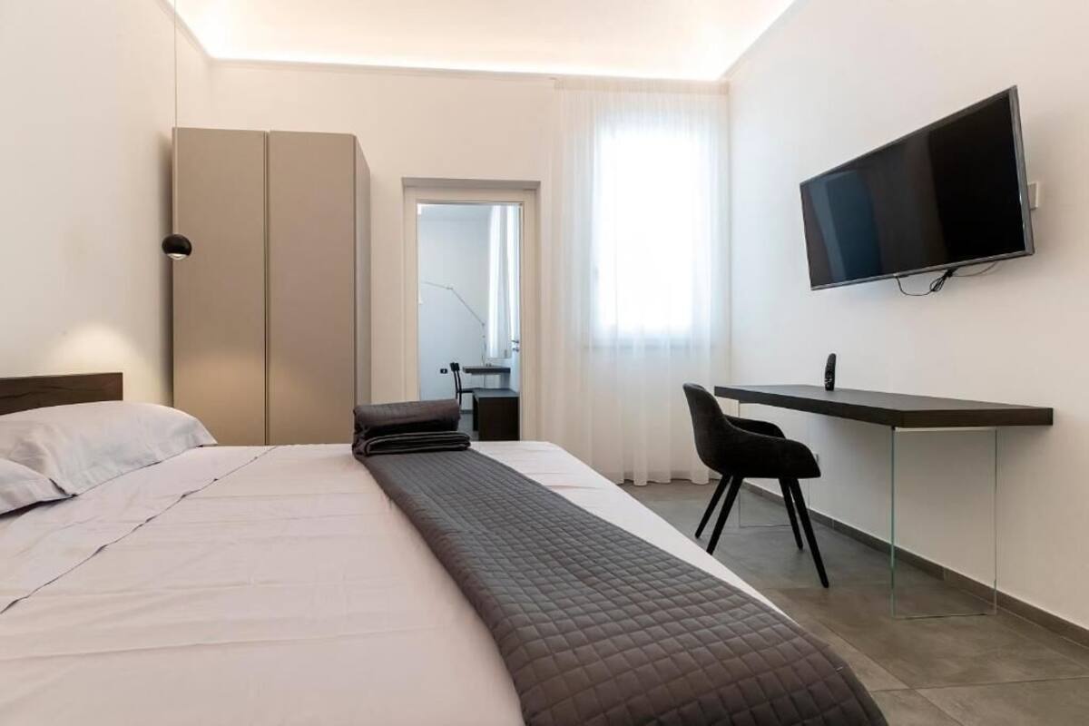 Una habitación de hotel con cama, escritorio, silla, televisor y armario.