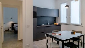 A modern kitchen with dark cabinets, a black microwave, and a dining area with a table and chairs. - 32VENTI (Trapani)