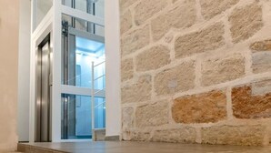 A modern interior with a stone wall and a glass elevator door. - 32VENTI (Trapani)