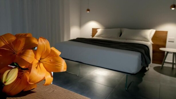 A modern bedroom with a bed, bedside tables, and a wooden nightstand. - 32VENTI (Trapani)