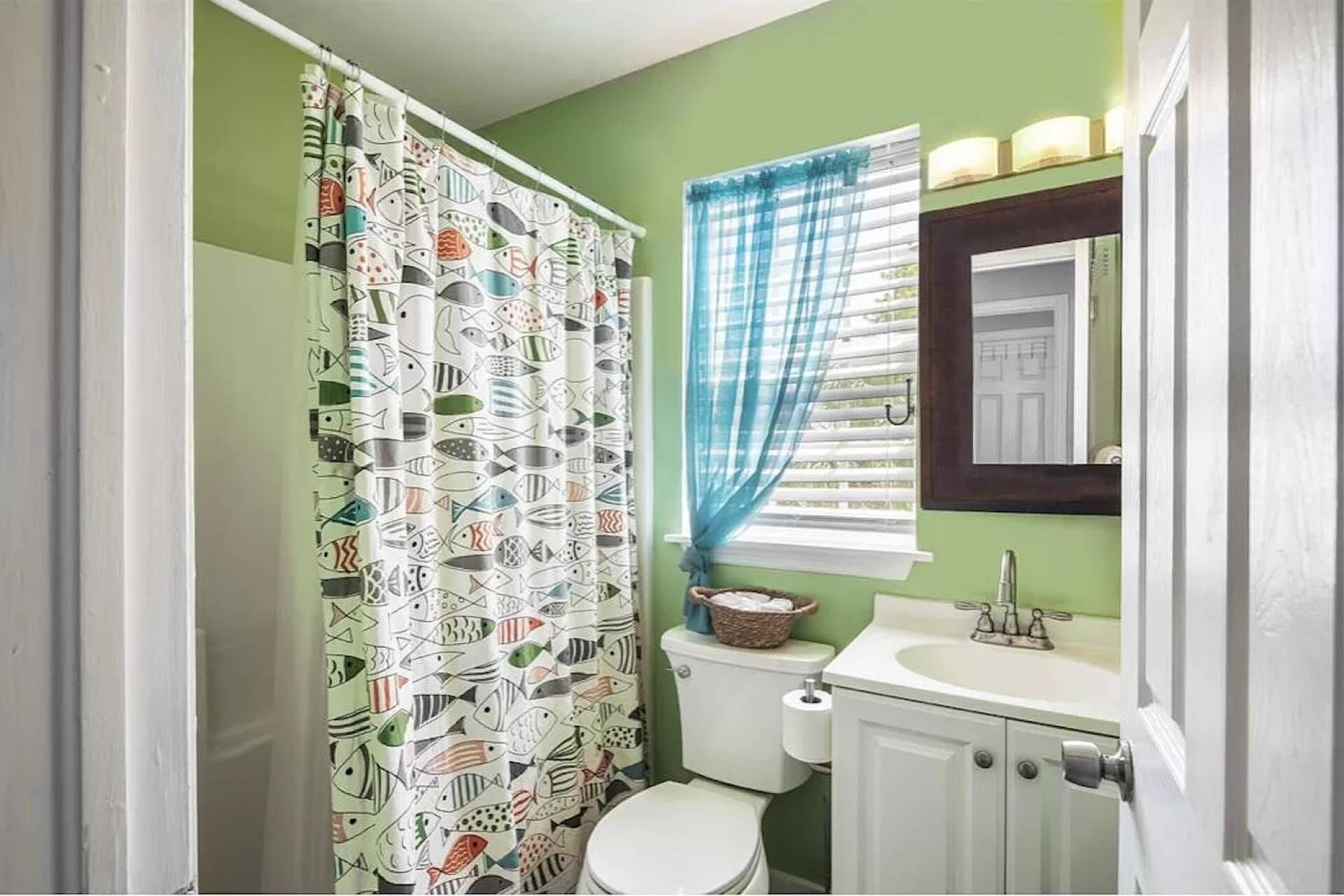 A bathroom with a toilet, sink, and shower curtain with a fish pattern.