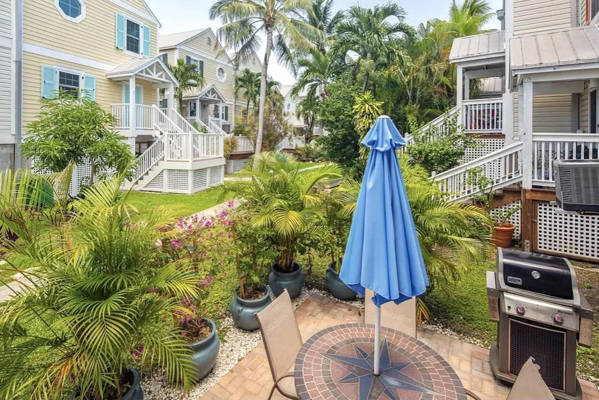 A backyard with a grill, a blue umbrella, and potted plants.