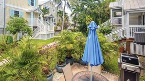 A backyard with a grill, a blue umbrella, and potted plants. - Castaway Cove: Charming 2BR Townhome in New Town, Key West with Shared Pool, Private Patio & Kayaks! (Key West)