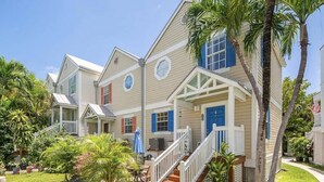 A row of two-story houses with a porch, a staircase, and a small garden with potted plants. - Castaway Cove: Charming 2BR Townhome in New Town, Key West with Shared Pool, Private Patio & Kayaks! (Key West)