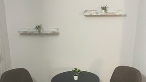 Une petite pièce avec deux chaises grises, une table ronde et deux étagères blanches ornées de plantes.