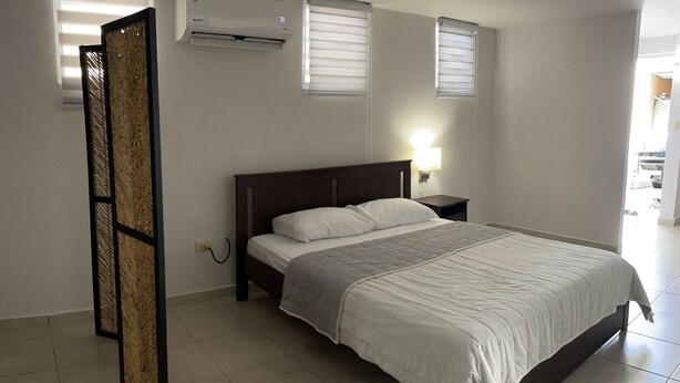 Une chambre à coucher comprenant un lit, un appareil de climatisation et une table de chevet avec une lampe.