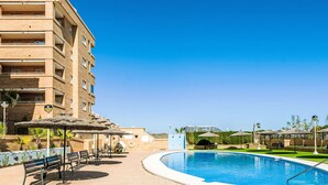 Ein Pool mit gewölbter Kante, umgeben von einer Rasenfläche und einem Gebäude mit mehreren Balkonen.