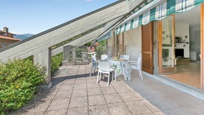 A patio with a table and chairs, a covered area, and a view of a building. - Appartamento Alessandra: Terrace and Lake View, Laveno Mombello, Italy (Laveno Mombello)