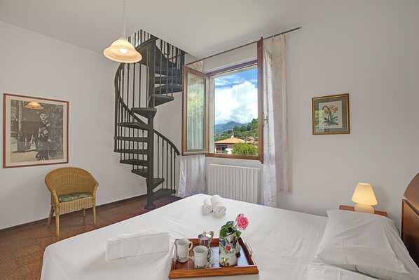 A hotel room with a bed, a chair, a tray with breakfast items, a window with a view, and a spiral staircase. - Appartamento Giulia, Laveno Mombello, Italy (Laveno Mombello)