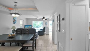 A spacious dining area with a dark wooden table and chairs, a ceiling fan, and a large window providing natural light. - Canal-Front Escape with Private Pool & Game Room in Port Charlotte - Point Of Rocks (Port Charlotte)
