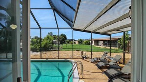 A pool area with a glass enclosure, sun loungers, and a view of a golf course. - Canal-Front Escape with Private Pool & Game Room in Port Charlotte - Point Of Rocks (Port Charlotte)