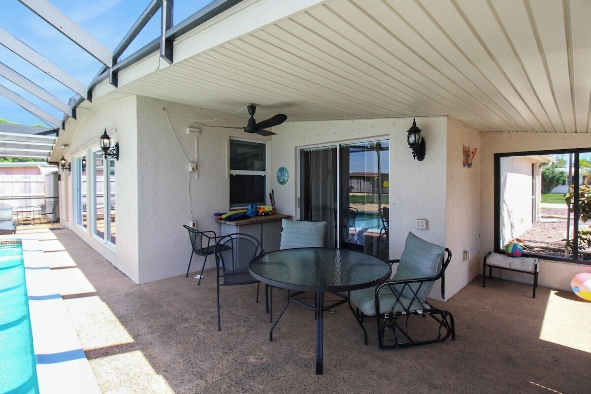 Un patio couvert avec une table et des chaises en verre, un ventilateur de plafond et une vue sur une piscine.