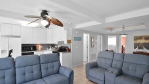A modern living room with two grey sofas, a ceiling fan, and a kitchen in the background. - Canal-Front Escape with Private Pool & Game Room in Port Charlotte - Point Of Rocks (Port Charlotte)