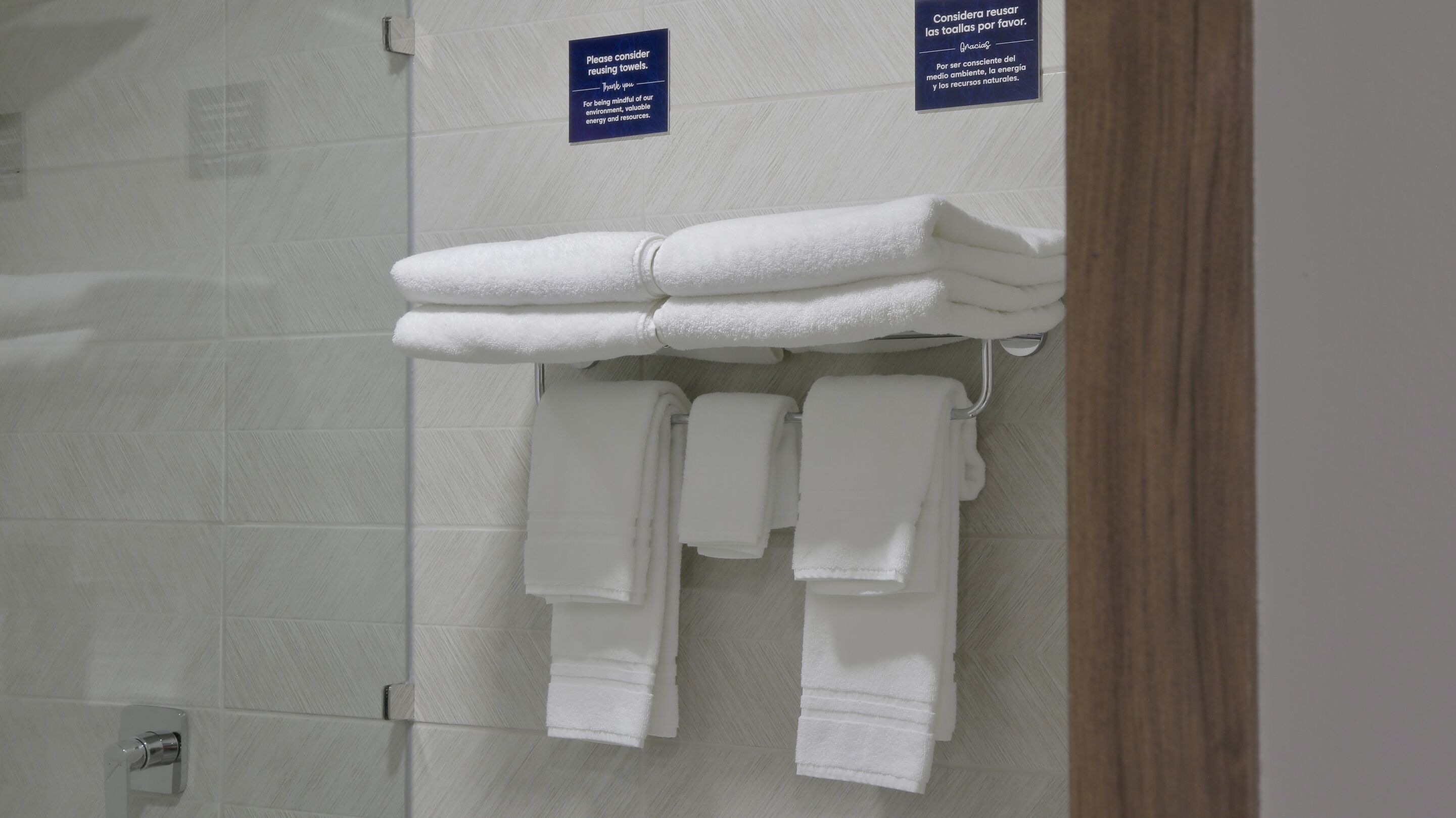 A bathroom with white towels hanging on a rack and a sign encouraging towel reuse.