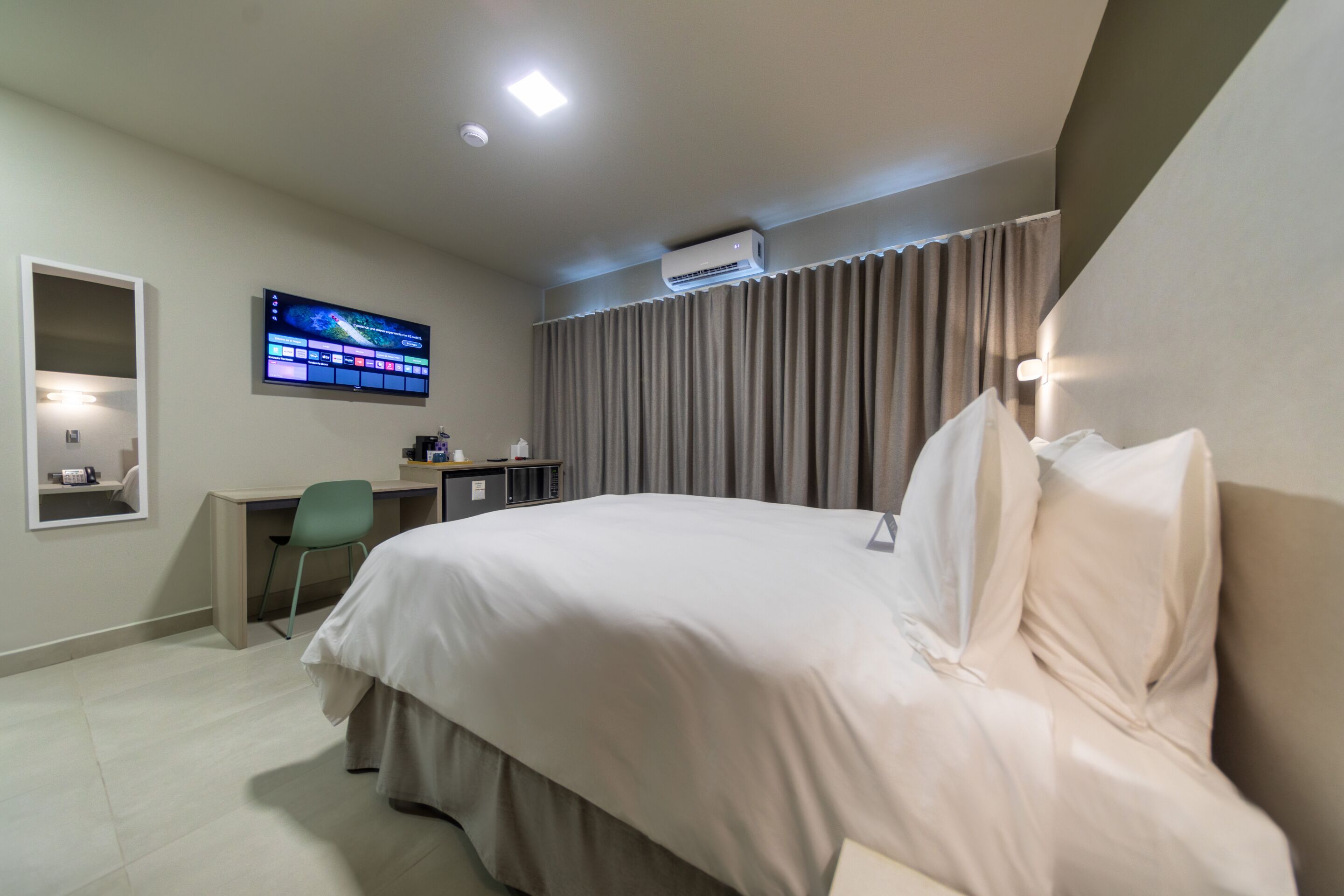 A hotel room with a bed, desk, chair, TV, and curtains.