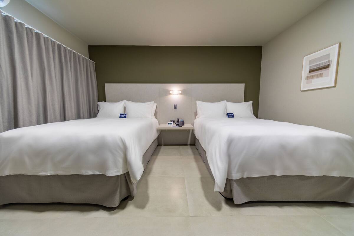 A hotel room with two single beds, a nightstand with a lamp, and a framed picture on the wall.