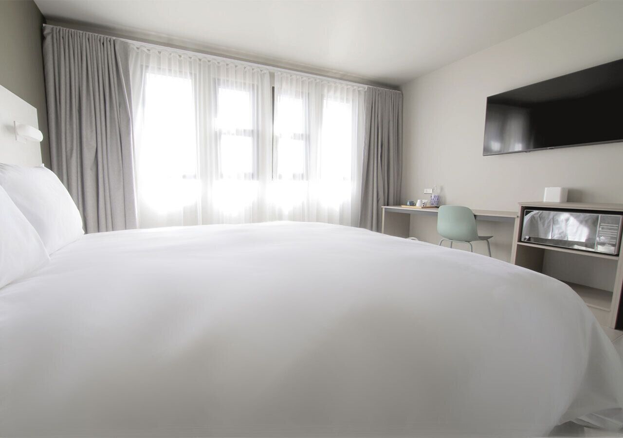 Een hotelkamer met een groot bed, een bureau, een stoel en een aan de muur bevestigde televisie.