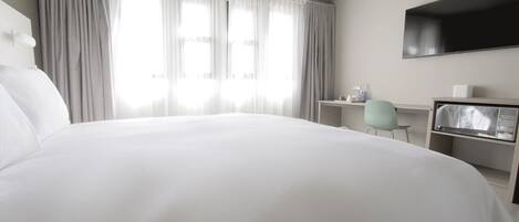 Een hotelkamer met een groot bed, een bureau, een stoel en een aan de muur bevestigde televisie.
