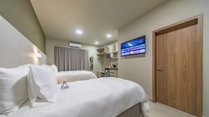 Ett hotellrum med två sängar, en tv som är monterad på väggen, en trädörr och ett litet skrivbord med en stol.