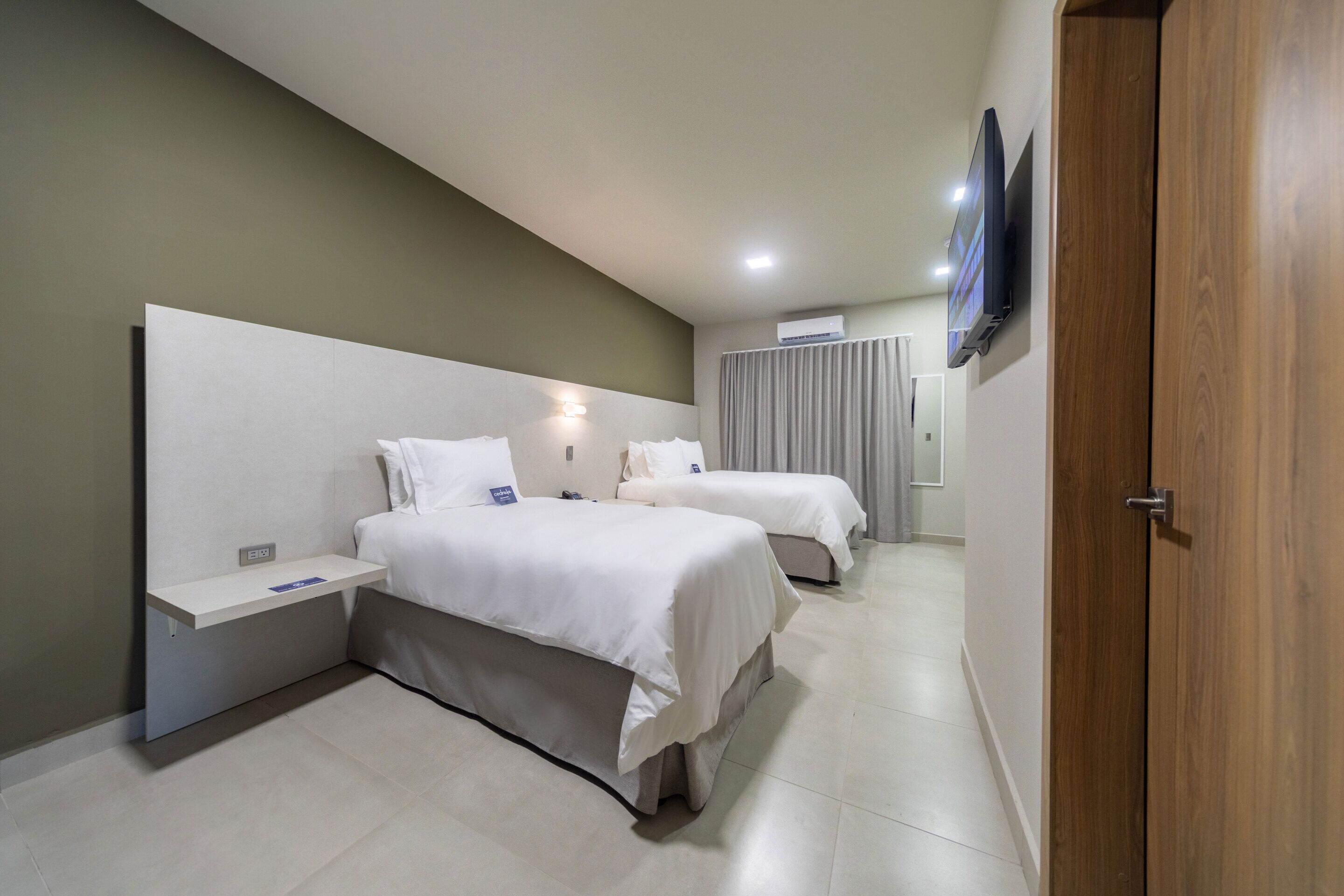 Habitació d'hotel amb dos llits, un televisor fixat a la paret i una porta de fusta.