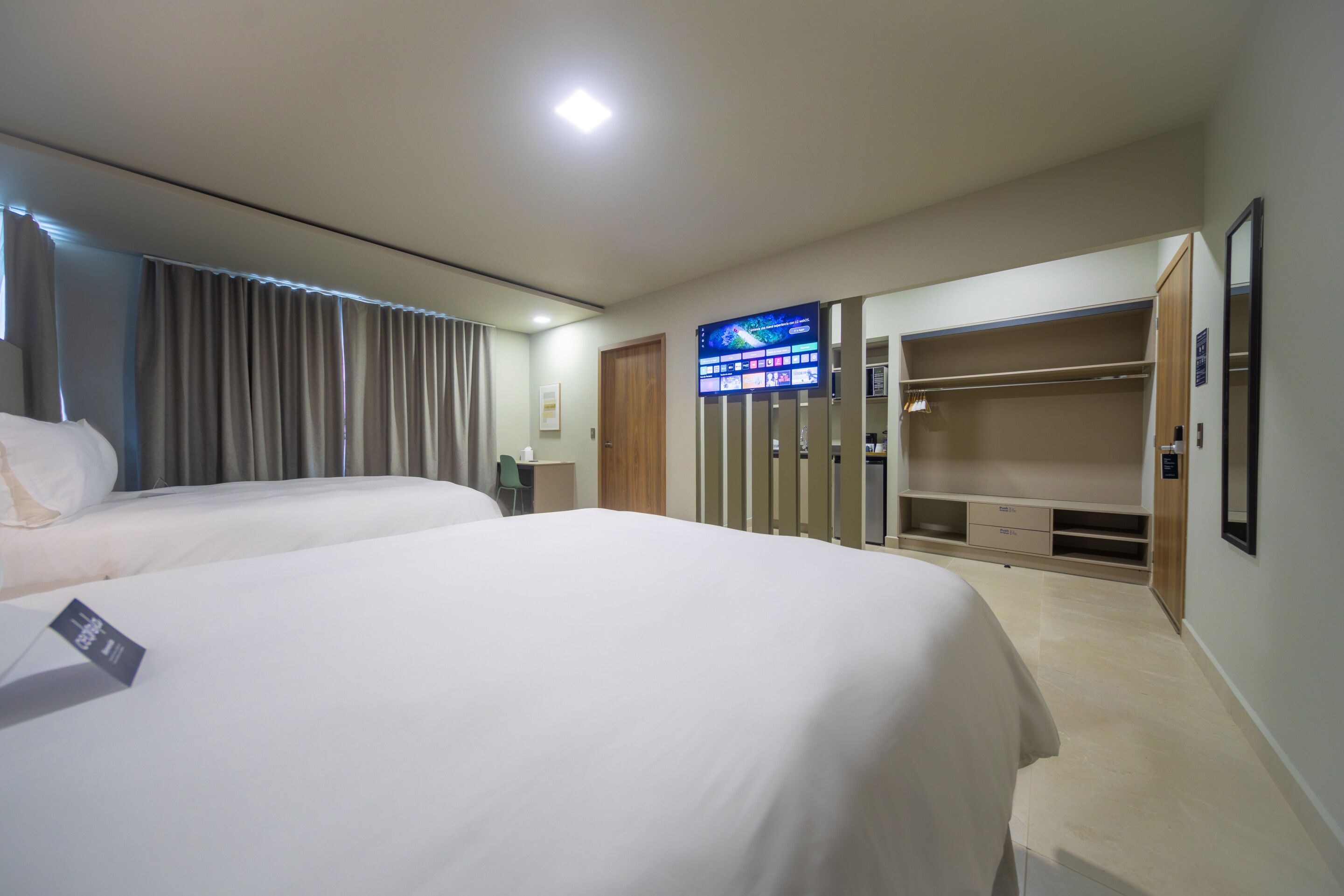 A hotel room with two beds, a TV, a desk, and a walk-in closet.