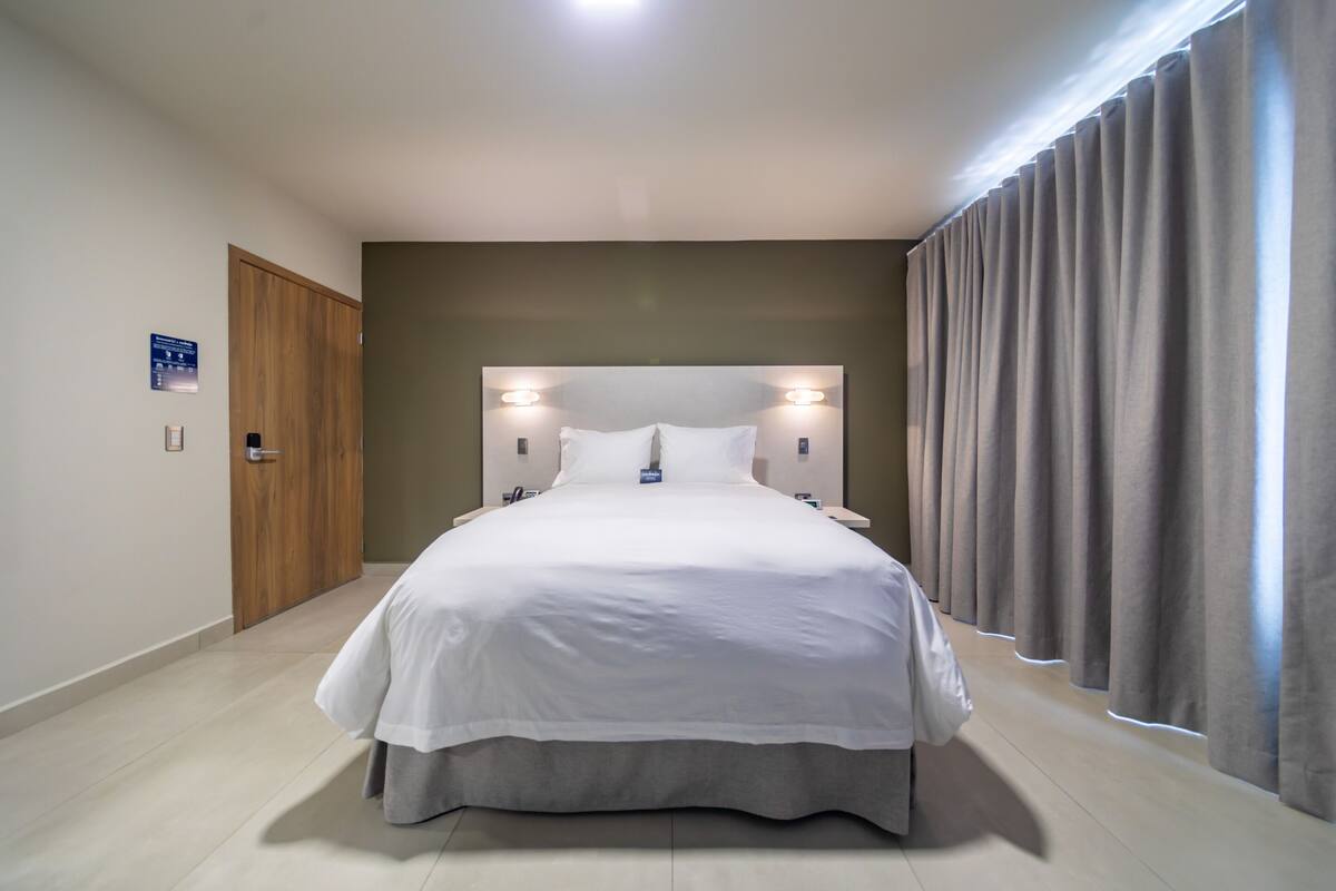 A modern hotel room with a large bed, a wooden door, and a view of the outside.