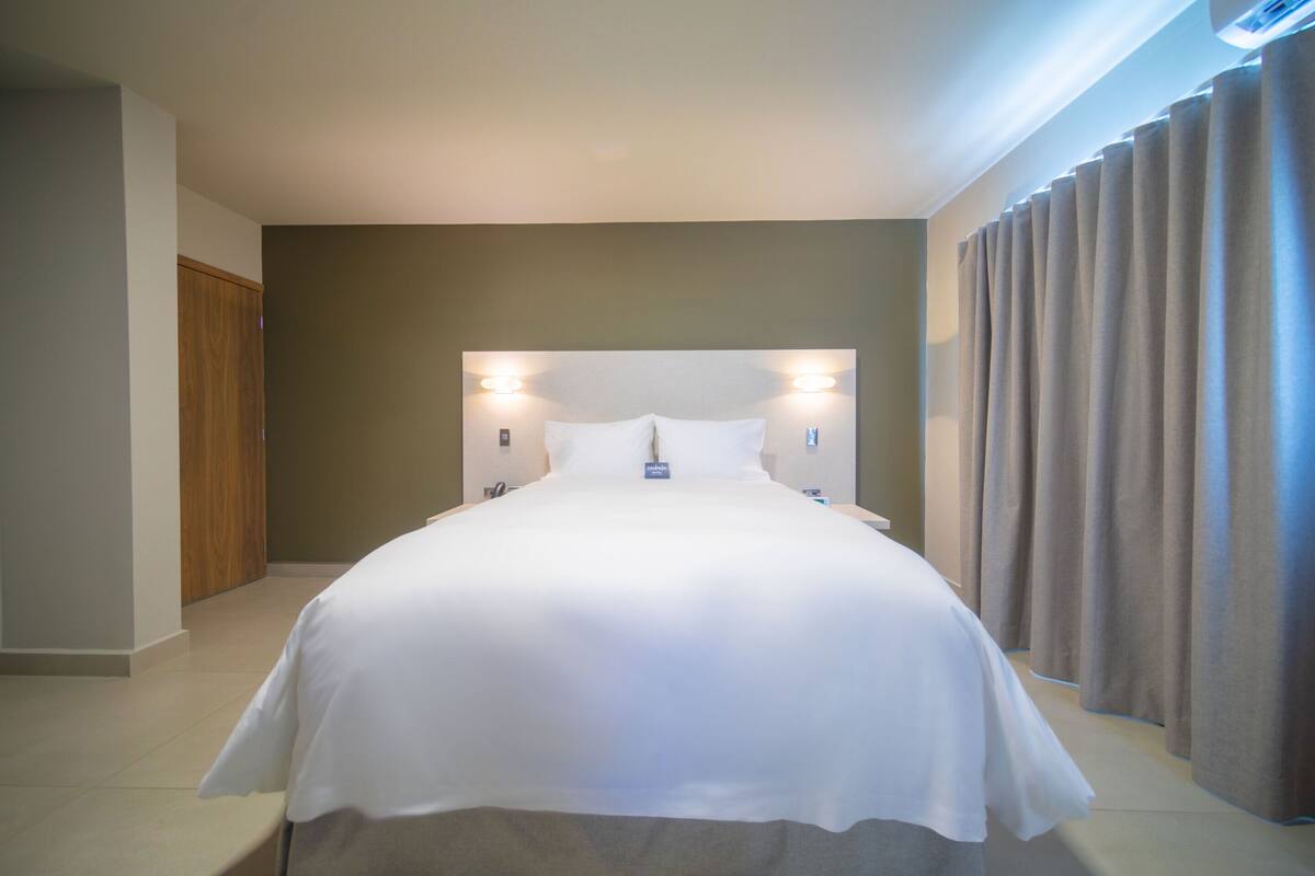 A hotel room with a large bed, two wall-mounted lights, a wooden door, and a curtain.