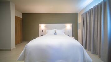 A hotel room with a large bed, two wall-mounted lights, a wooden door, and a curtain.