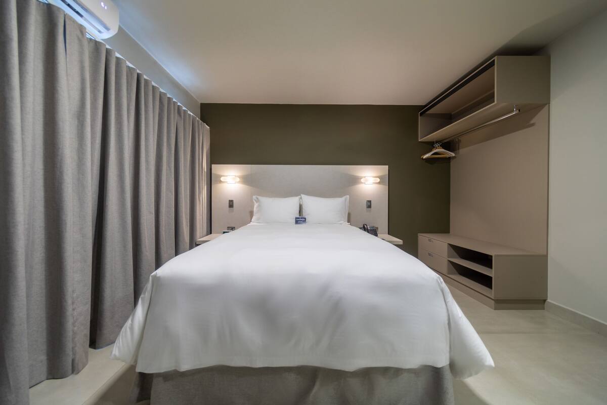 A modern hotel room with a large bed, a wardrobe, and a built-in air conditioning unit.