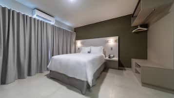 A modern hotel room with a large bed, a bedside table with a lamp, a built-in shelf, and an air conditioning unit.