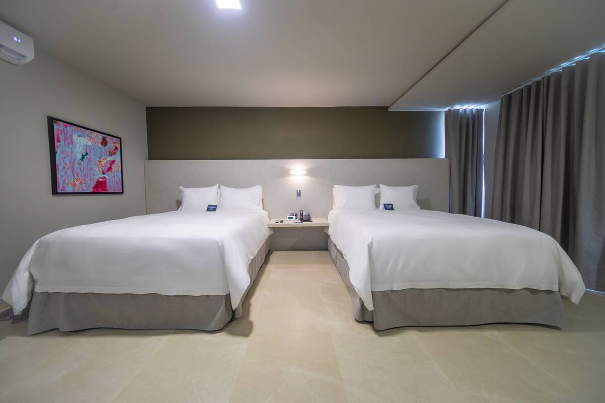 A hotel room with two beds, a nightstand, a painting, and a window with curtains.