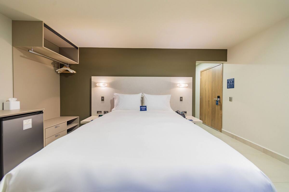A hotel room with a bed, bedside tables, a wardrobe, and a desk with a chair.
