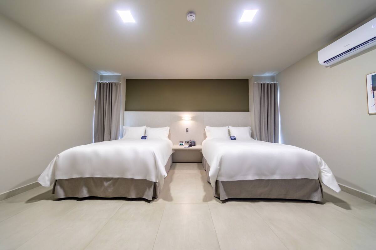 A hotel room with two beds, a nightstand, an air conditioning unit, and a headboard.