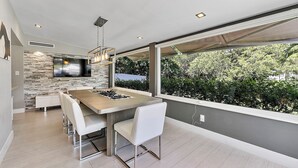 Una cocina moderna con una isla grande, sillas blancas y un televisor montado en la pared.