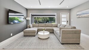 Una sala moderna con un sofá modular, una mesa de centro redonda y un televisor de pantalla plana montado en la pared.