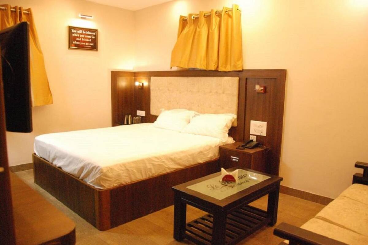 A hotel room with a large bed, a bedside table, a nightstand, and a small table with a glass top.