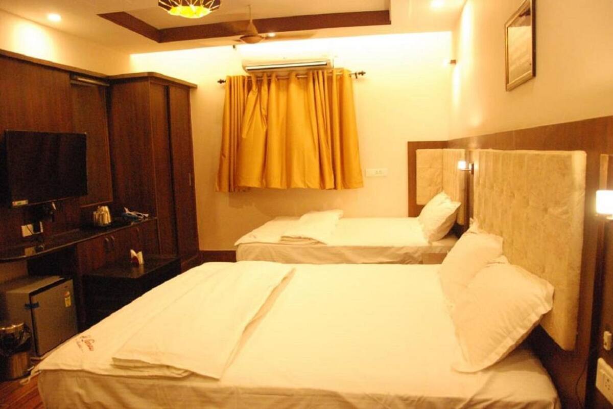 A hotel room with two beds, a TV, a wardrobe, and an air conditioning unit.
