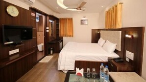 A hotel room with a bed, a TV, a desk, and a ceiling fan. - Le Emerald Residency (Chennai)