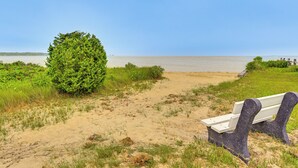 Ein sandiger Pfad am Strand führt zu einer Bank mit Blick aufs Meer.