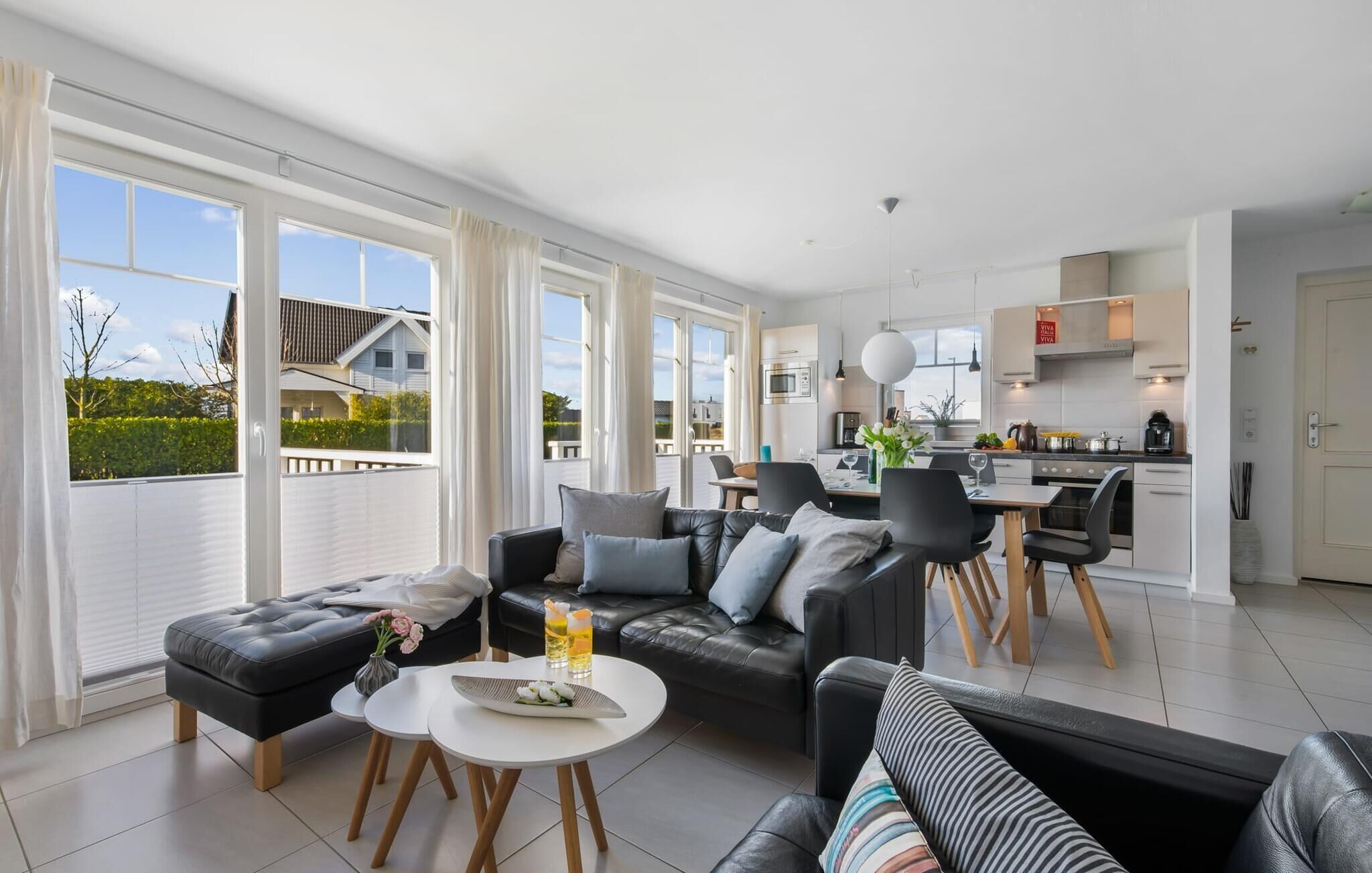 Een moderne woonkamer met een zwarte leren bank, een eettafel en een keuken op de achtergrond.