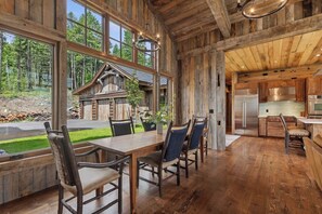 Un intérieur rustique en bois, comprenant un coin repas, une cuisine et de grandes fenêtres donnant sur une forêt.