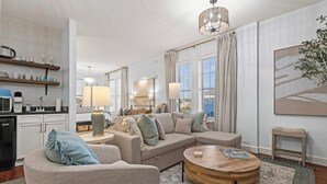 Una sala moderna con un sofá modular, una mesa redonda de centro y una cocina con microondas y estanterías.