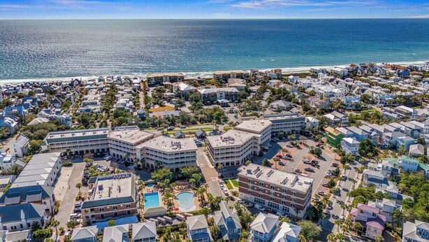 Vista aérea de un complejo turístico costero con varios edificios, una piscina y una playa al fondo.