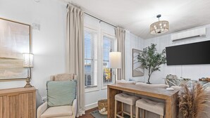 Una sala de estar moderna con una mesa de centro de madera, un sofá, un televisor montado en la pared y una ventana con cortinas.
