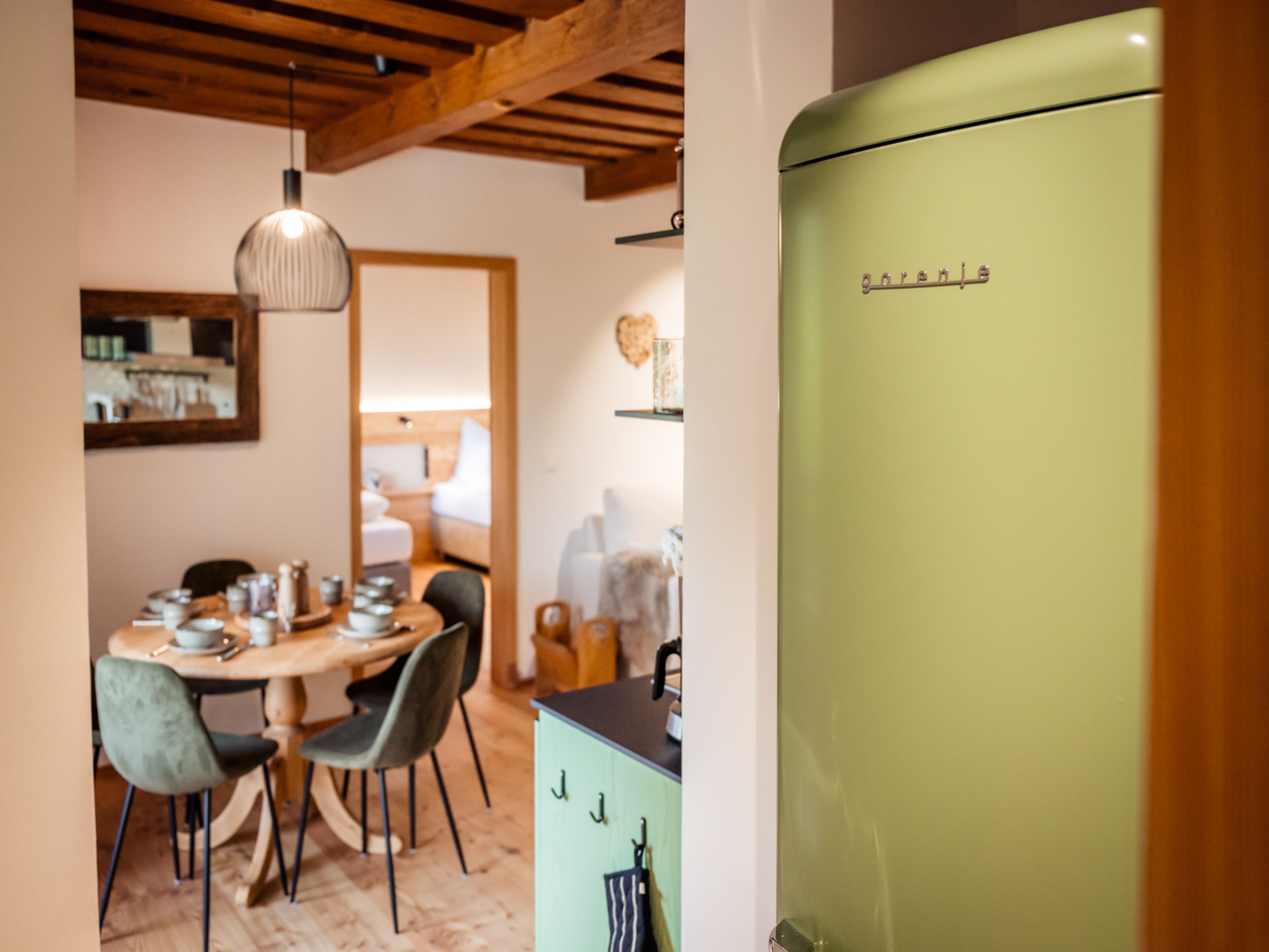 A dining area with a wooden table and chairs, a hanging light fixture, and a green refrigerator.