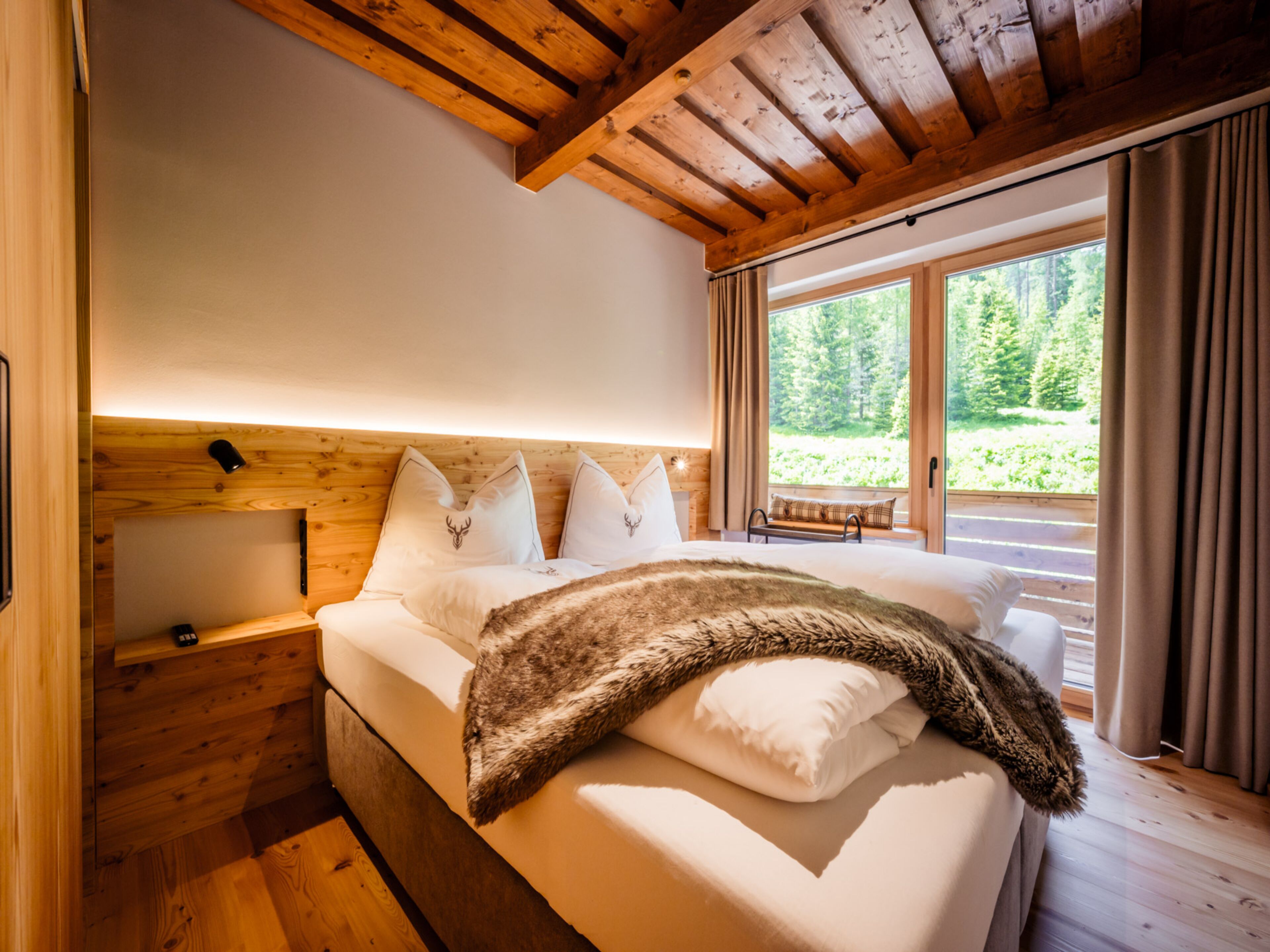 A wooden cabin bedroom with a bed, pillows, and a bench by the window.