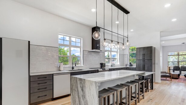 Una cocina moderna con una isla de mármol, taburetes de bar e iluminación colgante.