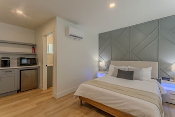 Unwind in style on the spacious queen-sized bed, complemented by a stunning accent wall that adds a touch of character to the room. The crisp, white linens create a peaceful ambiance, while the side tables feature mood lighting, wireless chargers, and USB